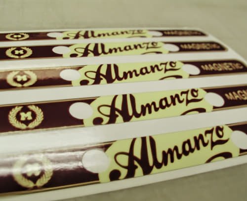 A sheet of custom die-cut strip stickers featuring the “Almanzo” logo in a maroon and cream color scheme. Ideal for branding promotional items, packaging, or giveaways.